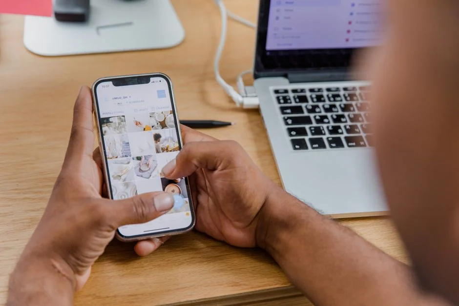 Hand holding smartphone with email app open, surrounded by books and laptop.